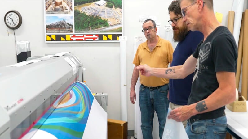 EPI-Colorspace team reviewing graphics beside a large-format printer.