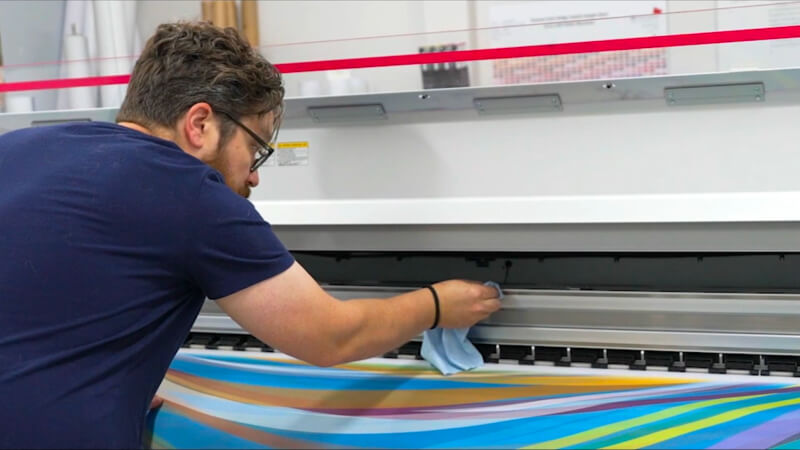 EPI-Colorspace team member cleaning a large-format printer during maintenance.