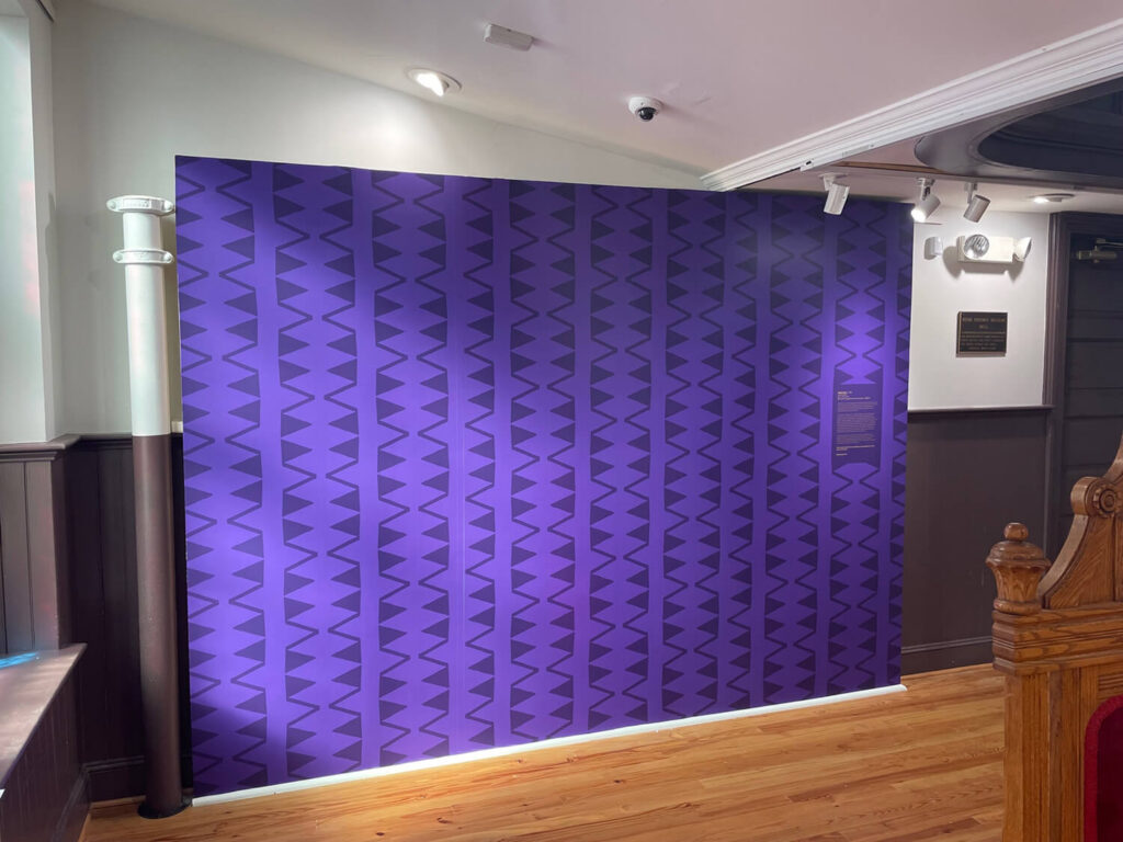 Purple patterned exhibit wall with repeating geometric panels.